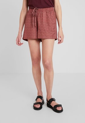Shorts maroon à motifs avec une taille élastique et un cordon de serrage. Tissu lisse, coupe décontractée et poches latérales. Portés avec des sandales noires.