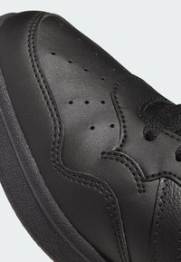 Baskets en cuir noir avec détails perforés, accents texturés et semelle en caoutchouc. Vue en gros plan mettant en valeur la couture et les lacets.