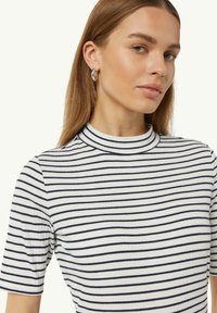 Gestreiftes, geripptes T-Shirt mit hohem Kragen; die Farben sind Weiß und Marineblau. Es verfügt über kurze Ärmel und einen weichen, strukturierten Stoff.