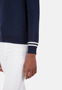Marineblauer Pullover mit Rippbündchen und weißen Streifen. Hergestellt aus weichem Strickmaterial, mit figurbetonter Form und minimalistischem Design.
