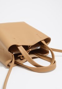 Borsa a tote in pelle marrone con texture liscia, apertura superiore e due manici lunghi. L'interno presenta una tasca con zip e cinturini aggiuntivi.