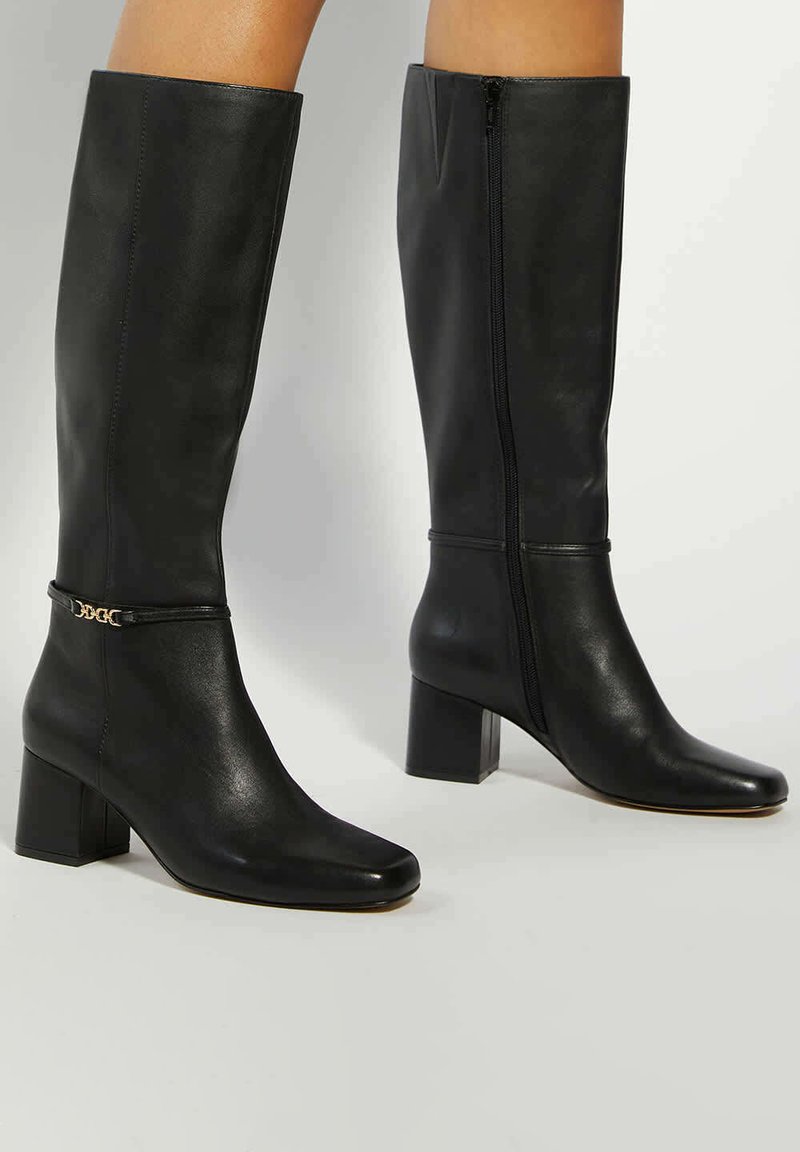 Black leather knee-high boots with a square toe, block heel, side zipper, and a decorative gold chain accent near the ankle.