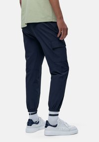 Marineblauwe cargobroeken met elastische boorden en zijzakken, gecombineerd met witte sneakers met marineblauwe accenten en geribbelde witte sokken.