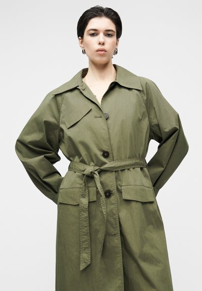 Χακί πρασινωπό παλτό τραντς από ελαφρύ ύφασμα. Διαθέτει γιακά, κούμπωμα με κουμπιά, ζώνη δέσιμο και δύο μπροστινές τσέπες.