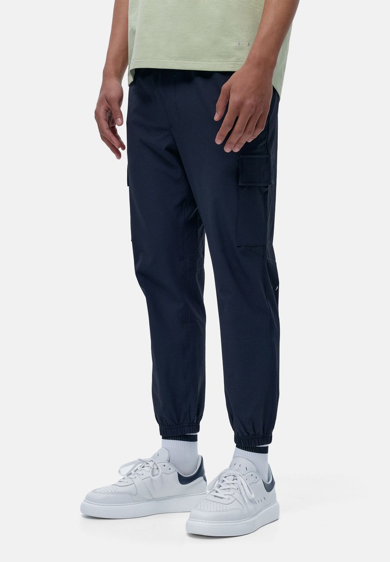 Marine cargobroek met elastische boorden, zijzakken en een ontspannen pasvorm. Gedragen met witte sneakers en een lichtgroen shirt. Soepele stofstructuur.