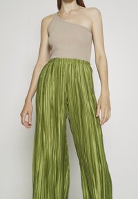 Beżowy prążkowany top na jedno ramię w połączeniu z zielonymi plisowanymi spodniami o szerokich nogawkach. Tkanina wydaje się lekka, o gładkiej i płynnej fakturze.