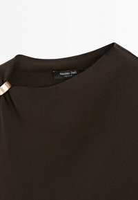 Mørkebrunt ribstrikket stoftop med rund halsudskæring og en lille gylden rektangulær spænde detalje nær kraven.