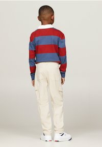 Vista posteriore di un bambino con un maglione a righe rosso e blu, pantaloni cargo crema con tasche e sneakers bianche con accenti blu navy.