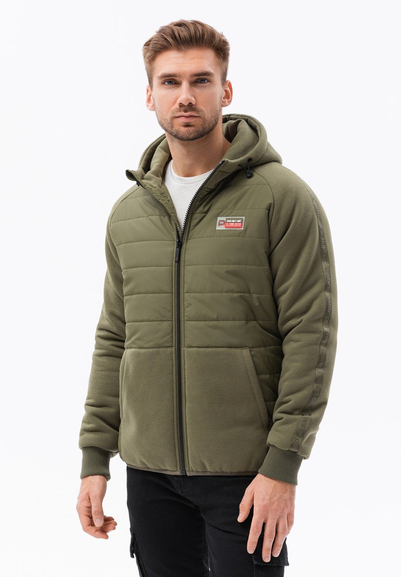 Giacca puffer verde oliva con cappuccio, caratterizzata da un frontale trapuntato, maniche lisce, zip frontale e patch con logo sul petto.