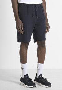 Pantaloni corti blu navy con vita elastica e cordoncino, realizzati in tessuto morbido. Abbinati a calzettoni bianchi e scarpe sportive nere.