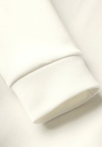 Witte katoenstof met een gevouwen manchet, een gladde textuur en een licht elastische rand. Eenvoudig ontwerp zonder patronen of accenten.