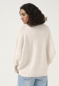 Pull en tricot beige clair à coupe ample, avec un motif texturé et de subtils sequins dispersés. Ourlet côtelé et manches larges.