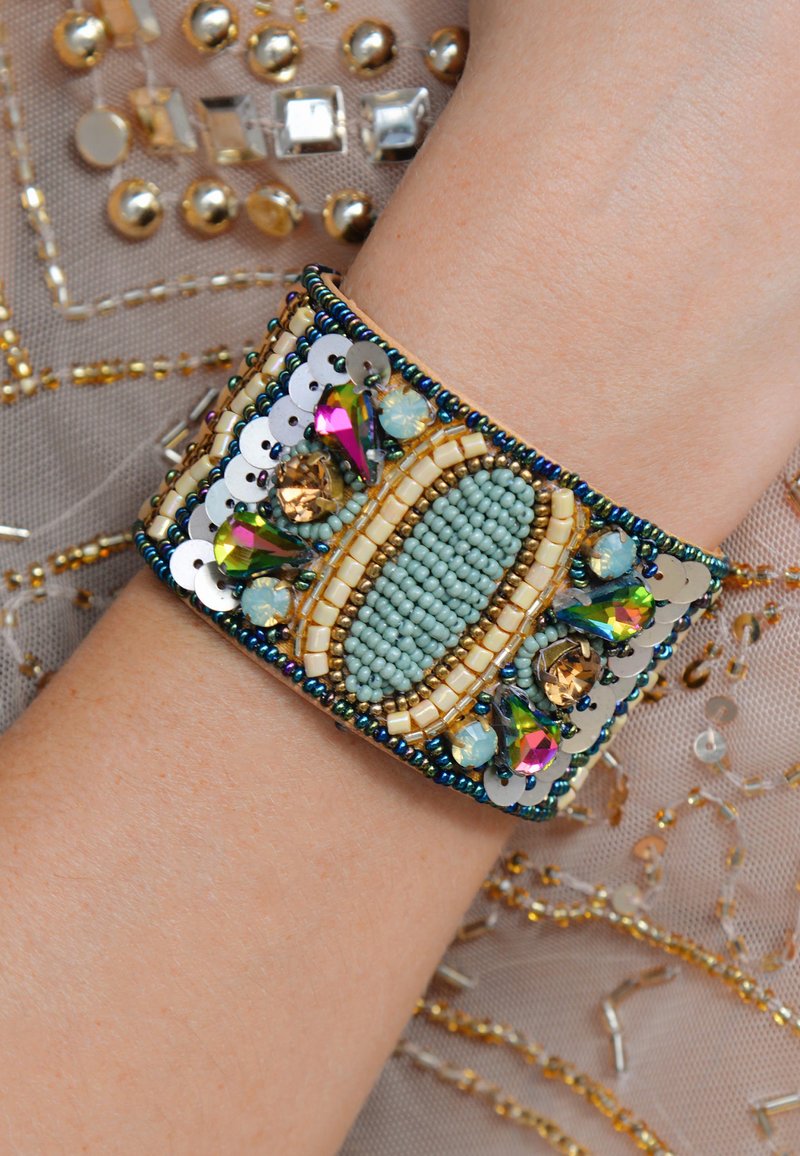 Bracelet coloré en perles avec des perles aqua, des accents dorés et des gemmes iridescentes. Conception de bracelet large avec des motifs et des textures complexes.