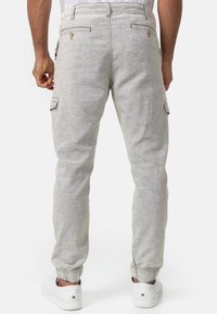 Helle graue Cargo-Hose aus strukturiertem Stoff, mit seitlichen Taschen, elastischen Bündchen und genähten Akzenten an der Taille und den Taschen.
