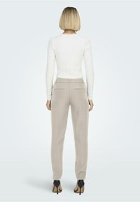 Pantalons beige clair sur mesure et haut blanc à manches longues en côtes. La tenue a une texture lisse et des détails de couture subtils.