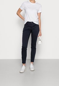 Námořnické skinny džíny s hladkým povrchem, doplněné o jednoduché bílé tričko s krátkým rukávem. Outfit doplňují tenisky s kulatou špičkou.