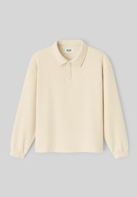 Polo beige à manches longues avec poignets élastiqués, col plié et patte de boutonnage cachée, présenté sur un fond gris.