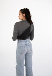 Un sac bandoulière noir porté en diagonale sur un haut gris à manches longues, associé à un jean taille haute bleu clair. Le tissu est lisse avec un léger éclat.