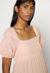 Vestido em rosa blush com decote quadrado, mangas bufantes e um tecido texturizado com riscas verticais. Silhueta fluida.