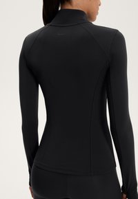 Maglietta atletica nera a maniche lunghe con colletto alto, design aderente, cuciture flatlock e discreto logo dettagliato sul collo. Tessuto liscio.