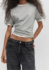 T-shirt grigio a maniche corte con bordi bianchi abbinato a jeans neri in denim a vita alta con elastico in vita e una leggera texture sbiadita.