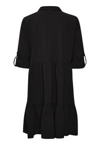 Schwarzes Kleid mit Hemdkragen, dreiviertel-langen Ärmeln und gestuftem Rüschensaum. Hergestellt aus einem weichen Stoff mit glatter Textur.