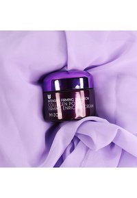 Lila Creme-Glas mit metallischem Finish und drehbarem Deckel, beschriftet mit "Intensive Firming Solution Collagen Power", auf lavendelfarbenem Stoff liegend.