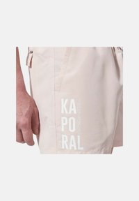 Shorts de bain rose clair en tissu lisse. Dotés d'une poche latérale et d'un texte de marque vertical blanc "KAPORAL JEANS." Coupe simple et droite.