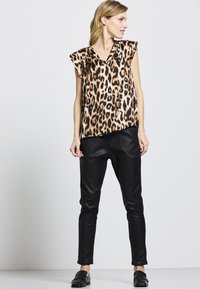 Bluse mit Leopardenmuster, kurzen Ärmeln und V-Ausschnitt; kombiniert mit schmal geschnittenen schwarzen Lederimitathosen und schwarzen Slippers.