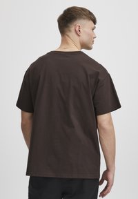 Brązowy bawełniany t-shirt o luźnym kroju, krótkich rękawach i okrągłym dekolcie, z gładką fakturą i minimalnymi detalami zszycia.
