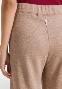 Bruine, glinsterende stretchbroek met een brede tailleband, voorzien van een klein label aan de achterkant. Glad textuur met een aansluitend ontwerp.