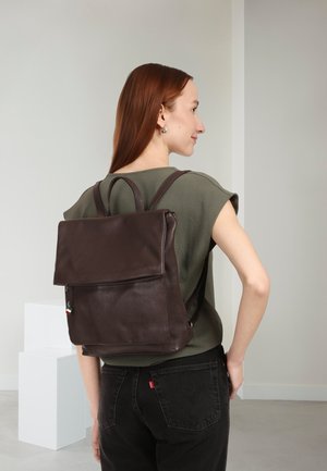 Brauner Leder-Rucksack mit glatter Oberfläche und Klappverschluss, ausgestattet mit verstellbaren Trägern und einem kleinen Detail in Form einer italienischen Flagge.