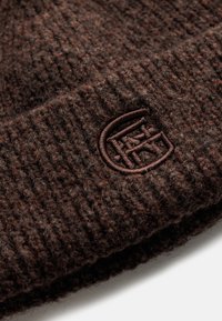 Brązowa dziana czapka wykonana z teksturowanej wełny. Posiada wystający, ciemnobrązowy naszywkę z logo z przodu. Żebrowany wzór zwiększa elastyczność.
