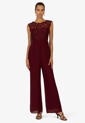 Burgunderfarbener Jumpsuit mit einem Spitzenoberteil, hohem Ausschnitt und weit geschnittenen Hosenbeinen. Verfügt über Falten und schwarze Riemchenhebel für den Kontrast.
