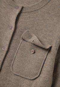 Cárdigan de lana marrón con cuello redondo, botones frontales y un bolsillo en el pecho izquierdo con un pliegue. Tejido texturizado y botones lisos.