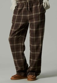 Pantalones de cuadros marrones con una cintura elástica, que presentan líneas en color beige claro. Tela suave con corte holgado, combinados con mocasines de color marrón claro.