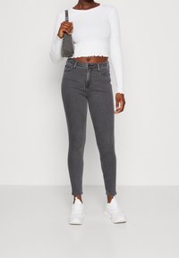 Vaqueros grises de tiro alto y ajuste Slim, con un lavado desvanecido y diseño de cinco bolsillos, combinados con una camiseta blanca cropped de manga larga.