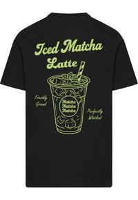 Black t-shirt featuring a green graphic of an iced matcha latte with a straw. Text includes "Iced Matcha Latte" and descriptive phrases.
