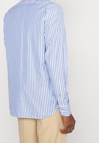 Blauw-wit gestreept shirt met lange mouwen, een afgeronde zoom, knoopmanchet en glad katoenstof. Voorzien van contrasterende verticale strepen.