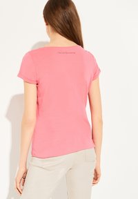 Lyserød kortærmet t-shirt med opsmøgede ærmer, buet nederste kant og en tekstdetalje på den øverste ryg. Fremstillet af blødt, letvægtsstof.