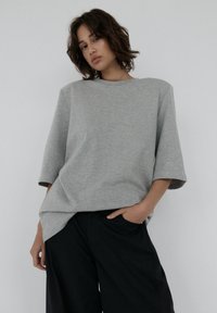 Szary, oversize t-shirt z krótkim rękawem, miękka tekstura i dekolt typu łódka, połączony z luźnymi czarnymi spodniami.