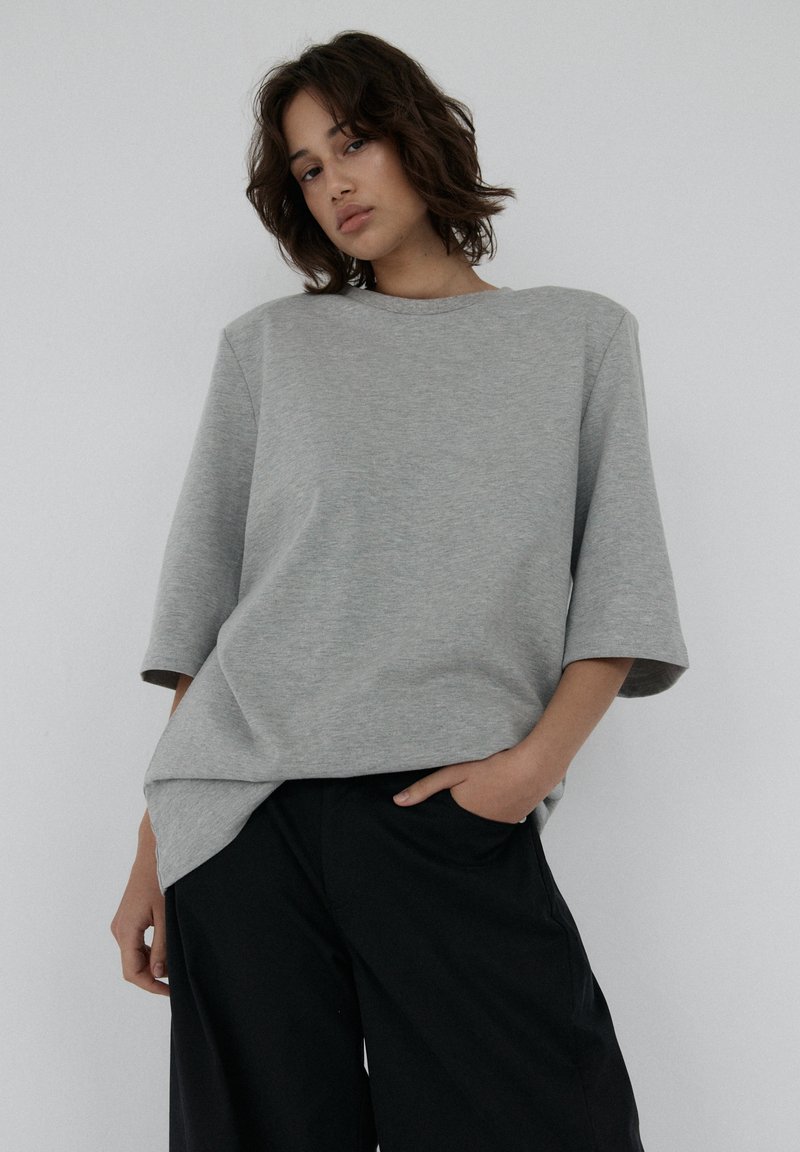 Szary, oversize t-shirt z krótkim rękawem, miękka tekstura i dekolt typu łódka, połączony z luźnymi czarnymi spodniami.