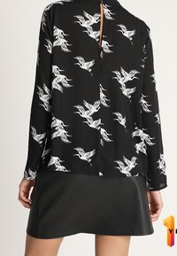 Svart blus med mönster av vita tranor, med långa ärmar och en nyckelhålsknappning bak, tillsammans med en svart läder minikjol.