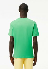 Camiseta de manga corta verde hecha de algodón suave, con un cuello redondo y un corte relajado. La vista trasera resalta un diseño sencillo.