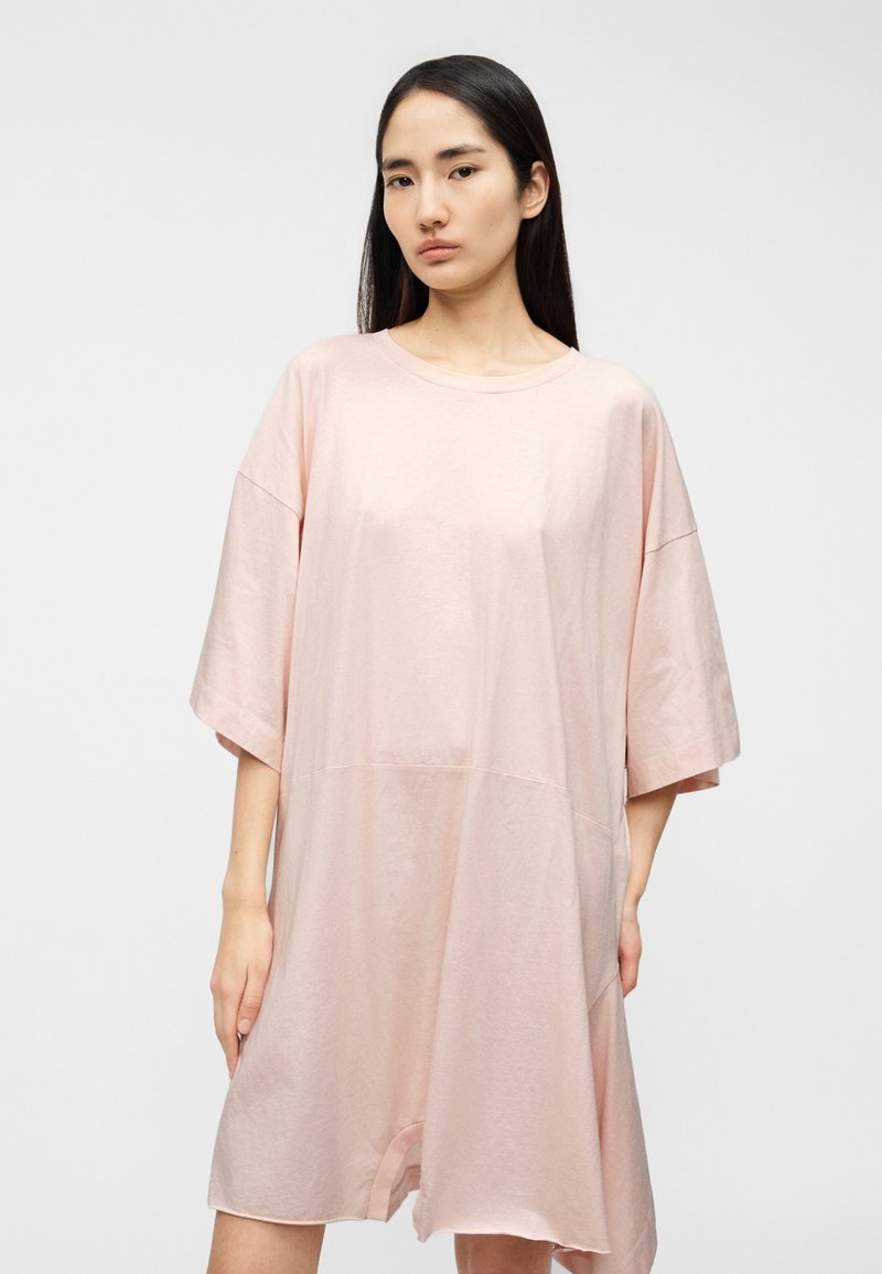 Robe ample à manches courtes en tissu rose pastel doux. Présente un col rond et une coupe décontractée, avec une taille légèrement basse.
