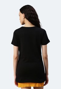 Schwarzes T-Shirt mit kurzen Ärmeln und rundem Halsausschnitt, aus weichem Stoff gefertigt, mit einem längeren Rückensaum und einem kleinen Logo-Tag an der Seite.