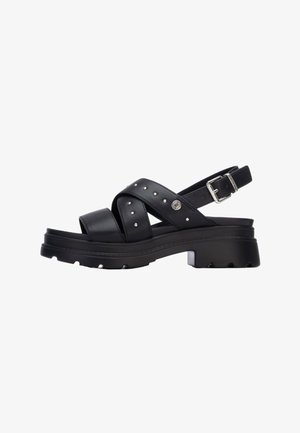 Sandalias de cuero negro con tiras cruzadas, detalles de tachuelas plateadas, cierre con hebilla y suela gruesa con relieves. Diseño ligero y duradero.