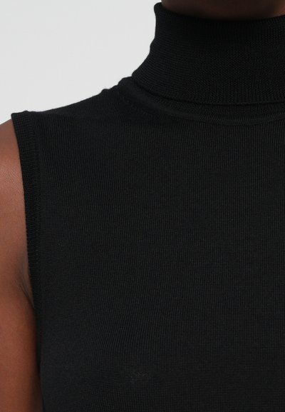 Mustat ribbed top ilman hihoja, jota käyttää tummaihoinen henkilö, näyttäen kaulan, olkapään ja ylärinnan alueen.