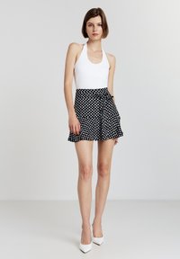 Body bianco con scollo halter abbinato a una mini gonna nera a pois con orlo arricciato e un fiocco in vita. Tacchi a punta bianchi.