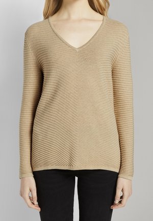 Maglione beige a scollo a V con una texture a coste, caratterizzato da una silhouette aderente e maniche lunghe, abbinato a pantaloni neri.